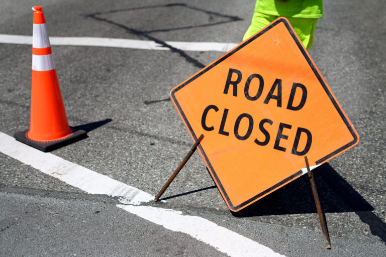 Road closed ahead traffic sign on the road with a body part of construction flagger