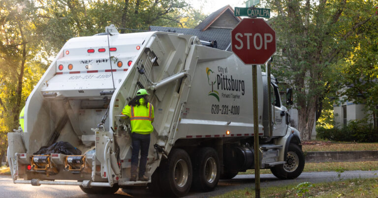 City of Pittsburg trash truck with an employee riding on the back.