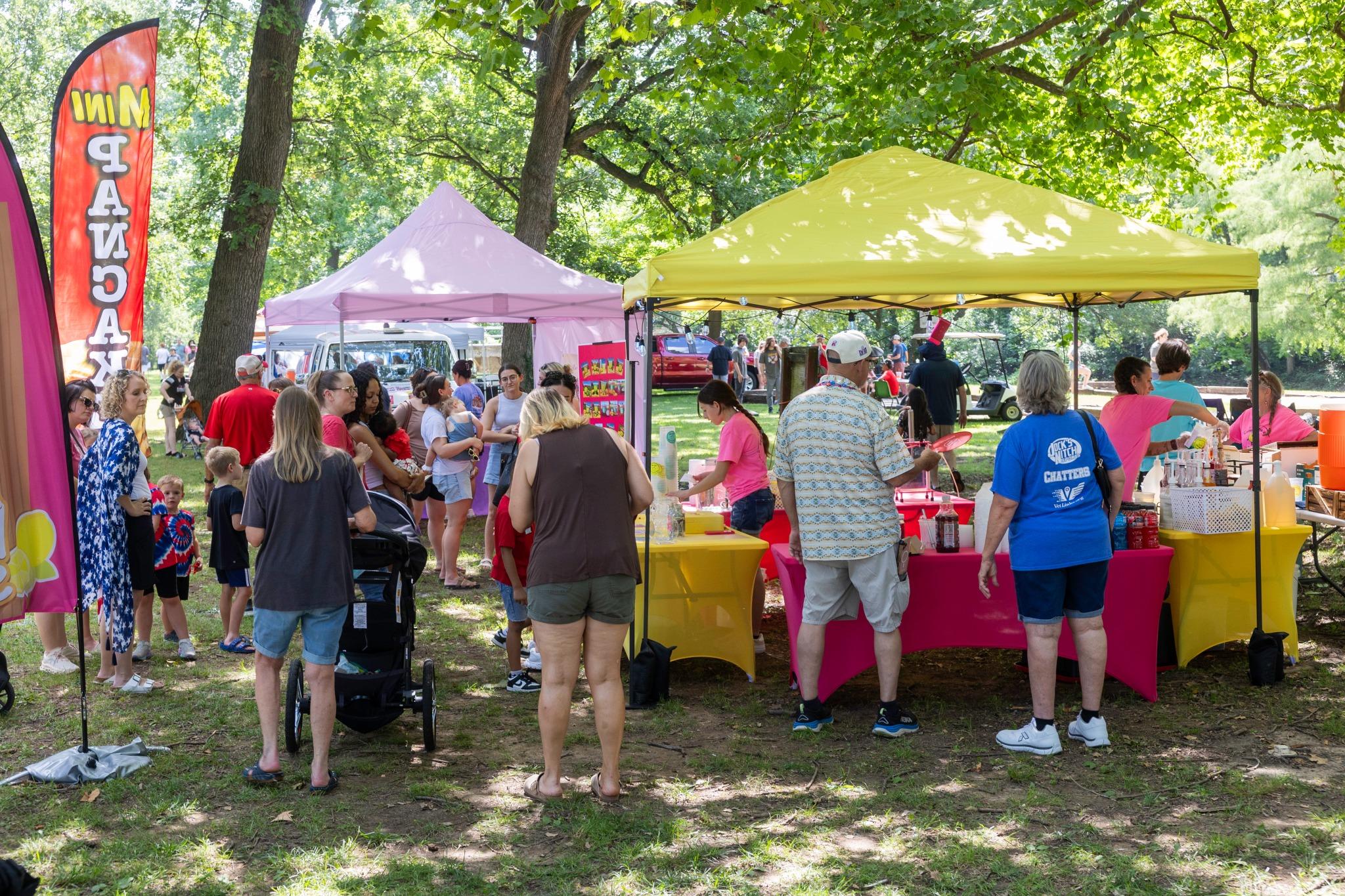 Outdoor event gathering with a large crowd and assorted stands with tent roofs.