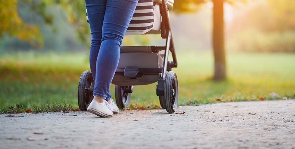 A woman walks with a stroller at a park.