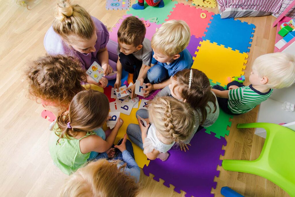 Group of kindergarten kids sitting closely on a floor together with teacher, providing group work.