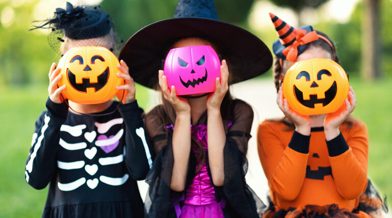 Children in Halloween costumes hide their heads behind pumpkin buckets outdoors